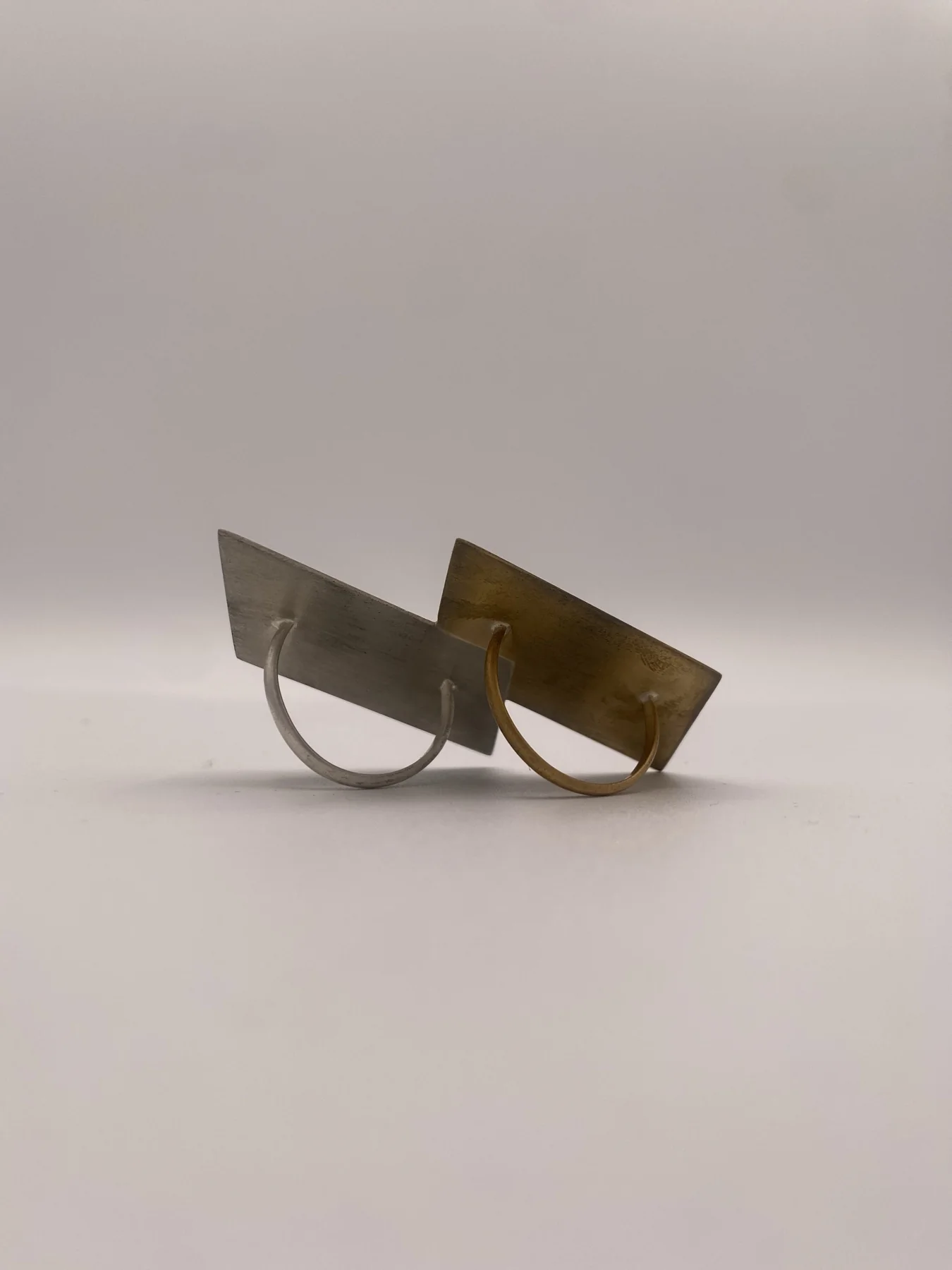 Pair of folded metal earrings resting on a pale surface.