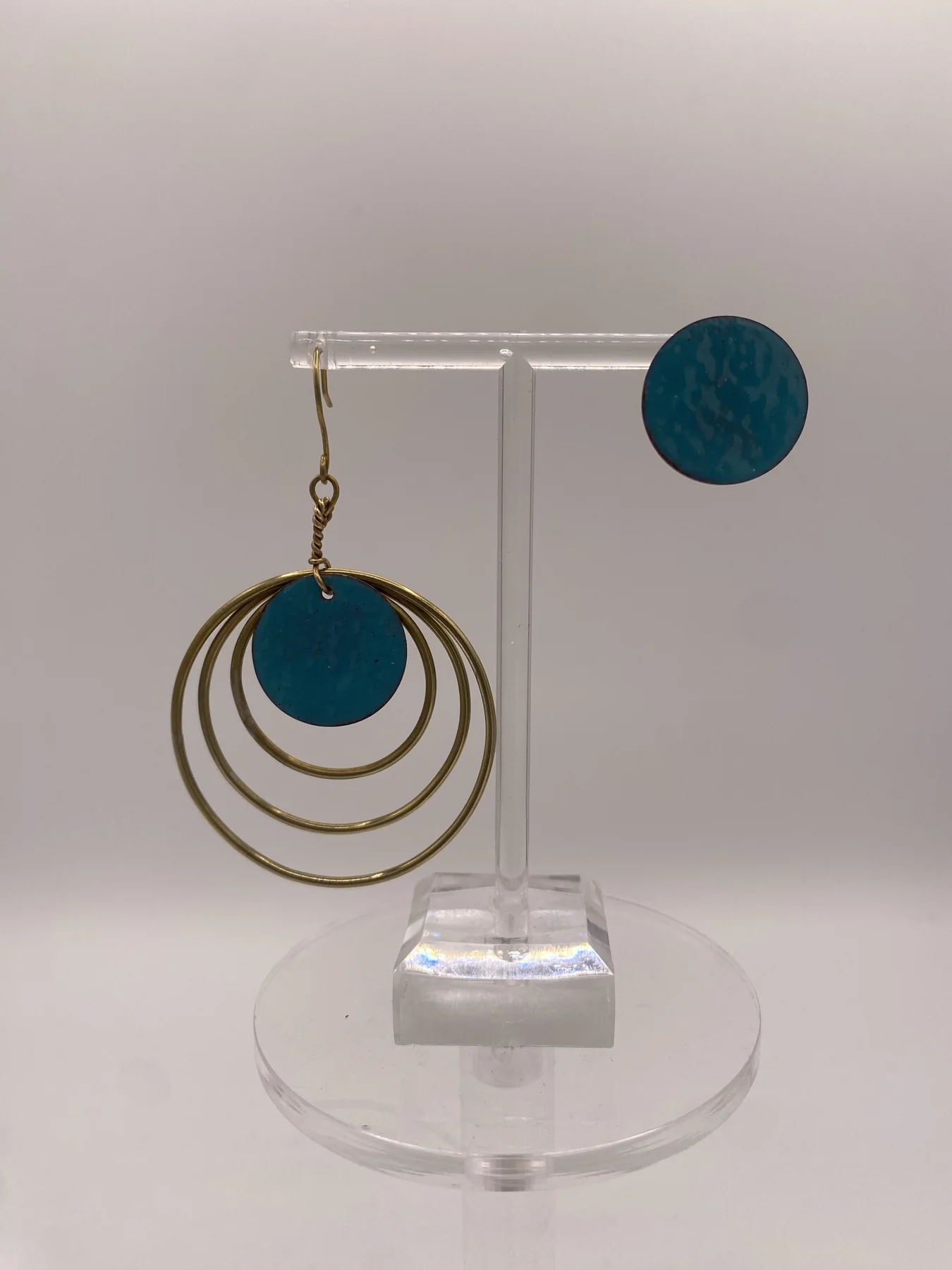 Circular drop earrings hanging from a clear display stand.